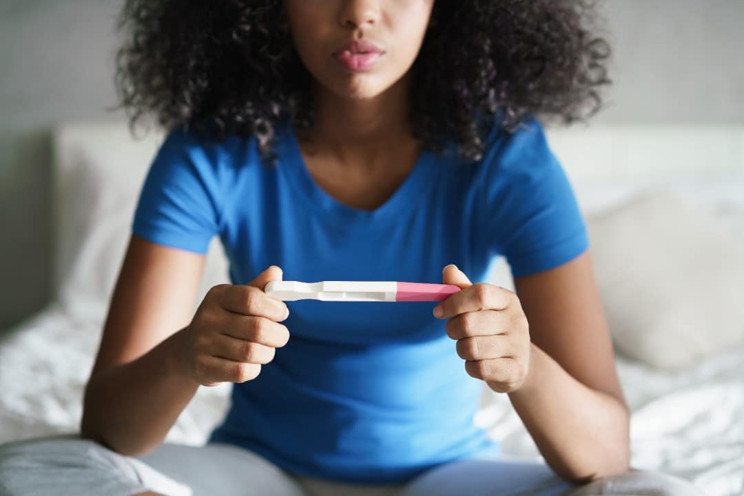 Black woman sitting on her bed holding a negative pregnancy test.